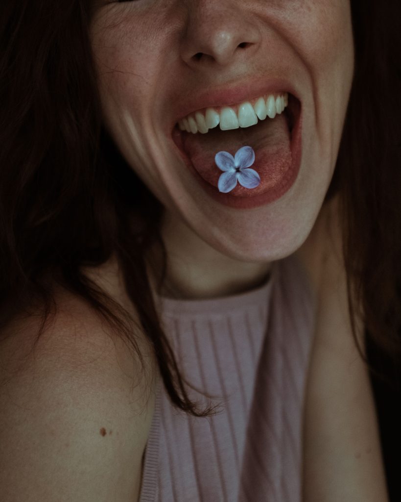 Artistic close-up portrait of a woman holding a lilac flower on her tongue, creating a delicate floral theme.